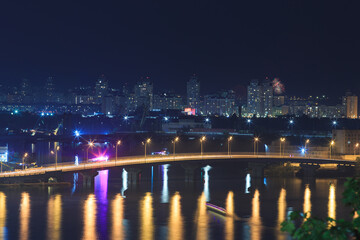 Car bridge over the river in a big city in a European city. Night landscape of a metropolis with a river, bridge and high-rise buildings.