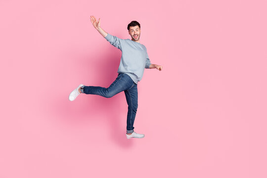 Full size photo of handsome young man jumping carry invisible shopping cart wave wear stylish blue outfit isolated on pink color background