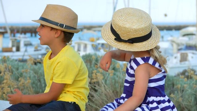 Little boy and adorable blond girl in hats sit together outdoors 
