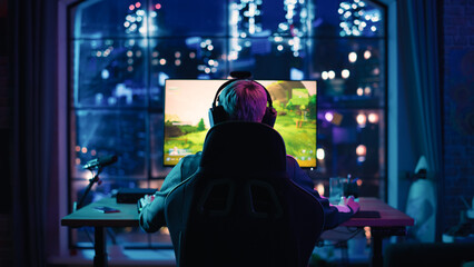 Back View: Professional Female Gamer Playing a Video Game on Personal Computer in a Neon Lit Living Room at Home. Girl Ready to Win Championship. Stylish Urban Apartment © Gorodenkoff