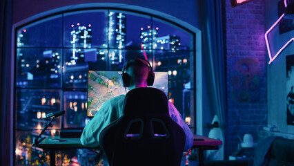 Fototapeta na wymiar Back of the Head Angle of a Successful eSports Gamer Playing a Video Game on Personal Computer in a Neon Lit Living Room at Home. Cozy Evening at Home in Loft Apartment.