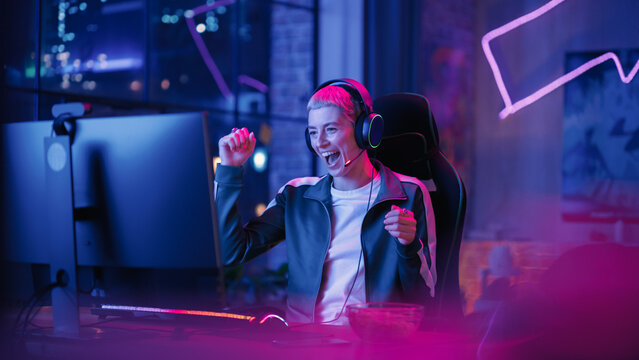 Successful Female Gamer Winning in Online Video Game on Computer. Portrait of Young Stylish Woman in Headphones Playing PvP Tournament with Other Players, Talking with Team on Microphone.