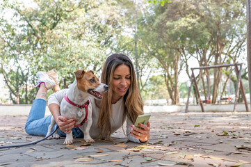 Jack Russell dog and woman holding cellphone in the park on a warm sunny day