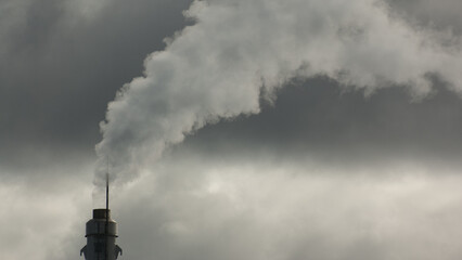 metal pipes of the plant against a gray sky, gray smoke comes out of the pipes
