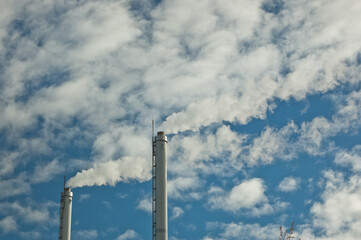 metal pipes of the plant against the blue sky, white smoke comes out of the pipes