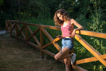 Young woman standing in the forest on a sunny summer day and using smart phone