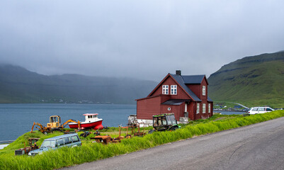 Haus auf den Färöer Inseln mit alten Landwirtschaftsmaschinen, Bagger, Boot, Traktor