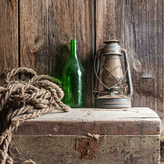 an old kerosene lamp in dust and cobwebs on an ancient wooden chest with a green empty bottle. wooden background.