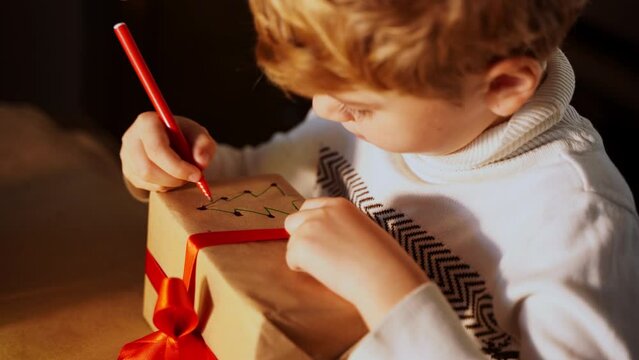 Close up child paints gift box New year present packaging. Making surprise for family. Dream. Children's paper craft school kindergarten. Christmas eve holiday party lights and ringing bells.