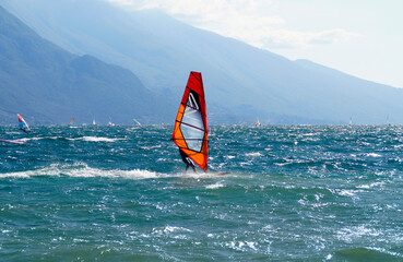 a surfer windsurfing on the turquoise waves of lake Garda by the mediterranean town Riva del Garda...