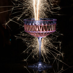 Glasses of champagne on blask background with sparklers. Pink sparkling wine. © Regina
