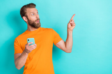 Fototapeta premium Portrait of impressed man look direct finger empty space hold telephone isolated on teal color background
