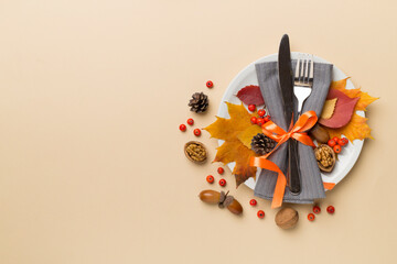 Plate with cutlery, napkin and autumn decor on color background, top view. Thanksgiving table setting