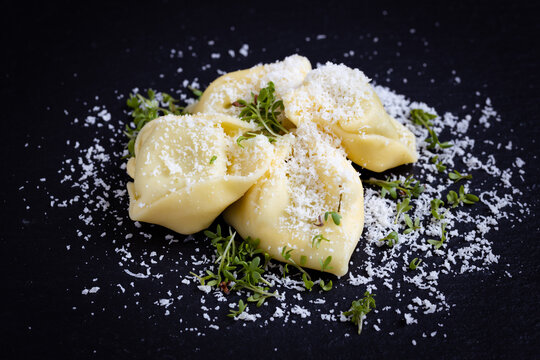 tortellini with Parmesan cheese on black background, photographed from the front