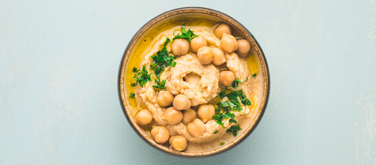 Hummus appetizer. Homemade hummus garnished with chickpeas,  parsley and olive oil and lemon, flat lay, light mint spring background, Middle east food, internet banner