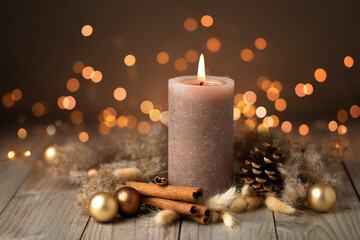 Warm colored natural Christmas Advent candle still life. Brown candle decorated with cinnamon sticks, pine cone, golden balls and dried grass in Boho style on rustic wood with Bokeh lights.