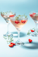 Glasses with cold pink champagne or punch with wine strawberries, ice and rosemary on blue background