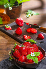Strawberries in clay bowl on a wooden table. Bowl filled with juicy fresh ripe red strawberries with cut berries close-up. Selective focus
