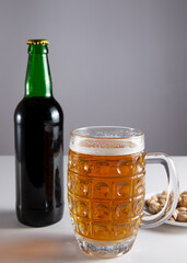 On the table is a glass of beer. Nearby is a bottle of beer and salty nuts.