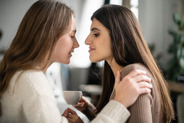 Side view of woman in sweater hugging partner with cup at home