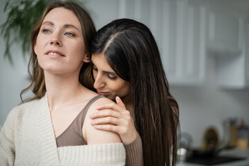 Young woman kissing shoulder of lesbian partner in kitchen