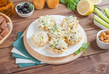 Tartlets stuffed with squid with cucumbers and corn with mayonnaise on a white plate on a dark wooden background