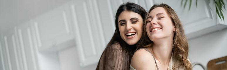 Cheerful lesbian women standing in kitchen at home, banner