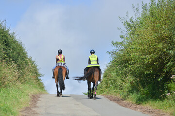 Riding over the hill, two horse riders riding their horses over the brow of a hill off on adventures with their horses on a summers day, wearing safety gear that makes them visible to other road users