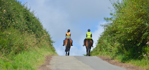 Riding over the hill, two horse riders riding their horses over the brow of a hill off on adventures with their horses on a summers day, wearing safety gear that makes them visible to other road users