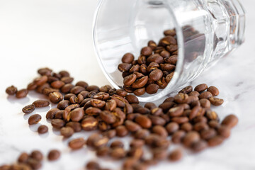 Roasted coffee beans spilled from the glass on the marble table