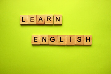 The word LEARN ENGLISH is made of wooden cubes on a yellow background. The concept of English language courses. Obtaining new knowledge, learning the language. Courses, training.