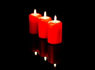 Three hot red candles arranged diagonally are reflected against the background of a black mirror.