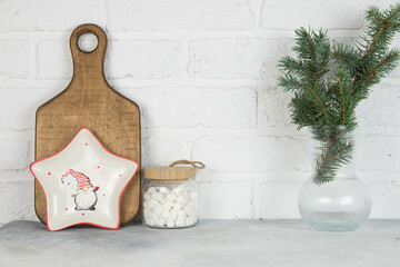 Christmas kitchen decoration- wooden cutting board, plate, marchmelloy are in glass pot, christmas fur tree in vase, star plate