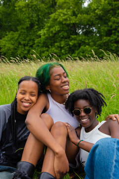 Three black non binary sat in the park talking and laughing.