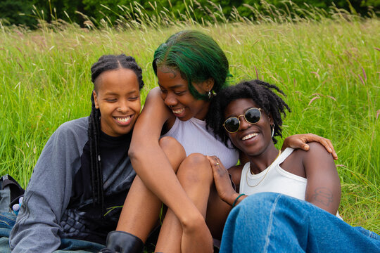 Three black non binary sat in the park talking and laughing.