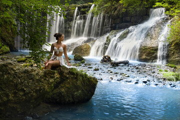 Frau im Bikini sitzt auf einen Stein vor dem wunderschönen Geratser Wasserfall in Bayern