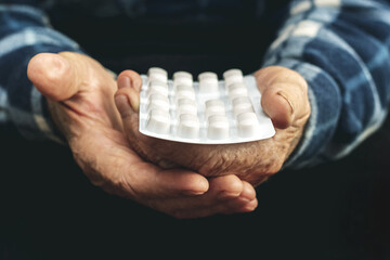 An elderly man holds pills in a blister pack in his hands. Taking pills to treat the disease