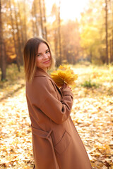 Happy young woman in a beige coast walks outdoors in autumn park, concept autumn. High quality photo