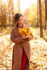 Happy young woman in a beige coast walks outdoors in autumn park, concept autumn. High quality photo