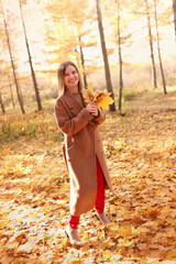 Happy young woman in a beige coast walks outdoors in autumn park, concept autumn. High quality photo