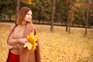 Beautiful elegant woman in autumn park holds an autumn yellow leaves near the face. Young woman in a beige coat walks outdoors in the park, concept autumn. High quality photo