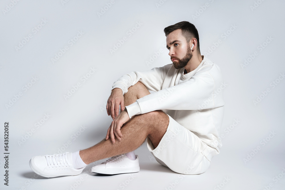 Wall mural Handsome man wearing white sweatshirt and shorts with wireless earbuds sitting - Wall murals