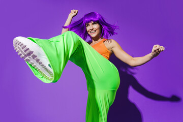 Carefree woman dancer wearing colorful sportswear having fun against purple background