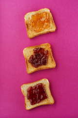 Slices of toast with strawberry, apricot and fig jam on pink