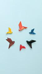 six paper origami pigeons different colors in circle fly away from white bird on light blue...