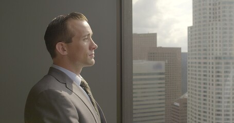 Successful, confident young business man looks across Los Angeles city skyline from Downtown office...