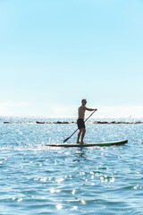 Plakat Young male surfer riding standup paddleboard in ocean.