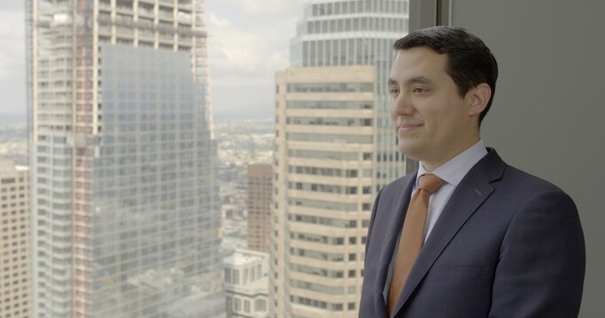 Successful young business man in suit and tie looks across Los Angeles from Downtown skyscraper window.  Medium close up, side view