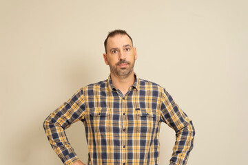 Fototapeta premium Cheerful bearded man in checkered shirt posing isolated on beige background, studio portrait. People lifestyle concept. Mock up copy space. Standing with your arms akimbo on your waist blinking.