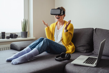 Excited young sitting on the sofa and using virtual reality headset at home